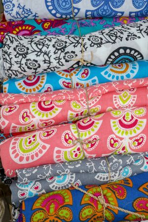 Rolled up colored fabrics tied with string. Shop with brightly colored sarongs. Sarung pantai ready...