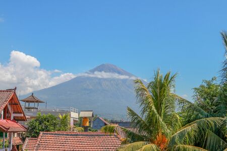 Tropical paradise with palm trees and majestic volcano in the background. White clouds around a...