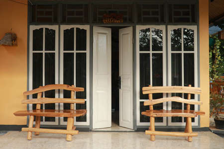 White glazed wooden door to the house. Wooden benches on the sides of the door. Wooden open door of a home. Front view of half-open door. Horizontal shot.の写真素材