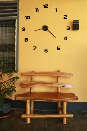 wooden bench near yellow wall. Vintage wooden bench under the wall clock.の写真素材