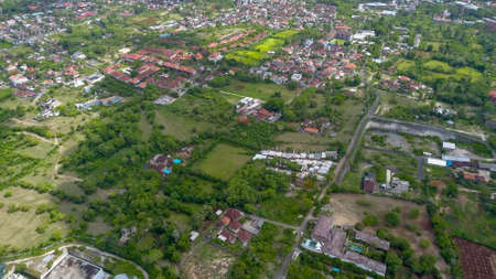 Many villas with brown-orange shingle roofs between tropical trees on the sky background in Ubud on Bali. Sun is shining onto them. Aerial photoの写真素材