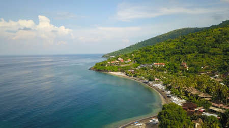 Aerial photo of a wild beach in Bali. A long strip of beach and a steep mountain slope covered with greenery. Wild beach in Bali with yellow sand and clear turquoise ocean waterの写真素材