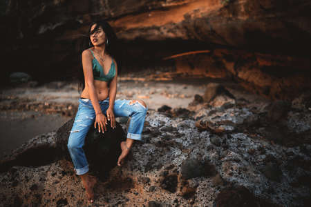 young asian woman wearing sexy clothes sitting on the rock during sunny summer day. Rocky backgroundの写真素材
