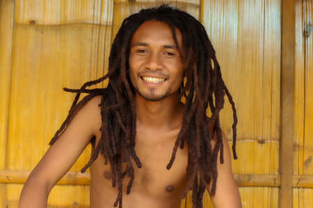 Close up of smiling indonesian guy man with dreadlocks with wooden in the backgroundの写真素材