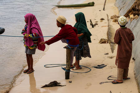 Labuan Bajo, Flores, Indonesia, 5 April 2021. children playing on the beach while helping their father pull the boat with ropesのeditorial素材