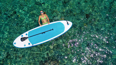 Aerial view of pretty woman lying on azure sea surface. Calm Relaxed Woman Resting in calm sea by Sup board. Funny summer water sports. Healthy Lifestyle. Surfing, Fashion. Summer Vacation. 4Kの写真素材