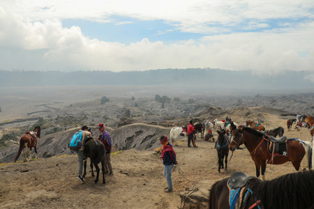 Mount Bromo, Indonesia, 28 May 2022. Group of Asian tourists with horses walking towards Mount Bromo in the morning with a Hindu temple in backgroundのeditorial素材