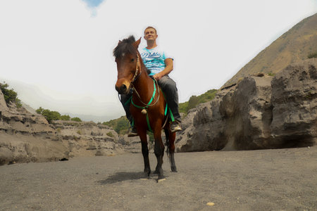 Mt.Bromo, Pasuruan, East Java, Indonesia - 28 May 2022. Man on horseback walking near Hindu temple Pura Luhur Poten situated at the foot of the volcano Bromo, Bromo Tengger Semeru National Parkのeditorial素材