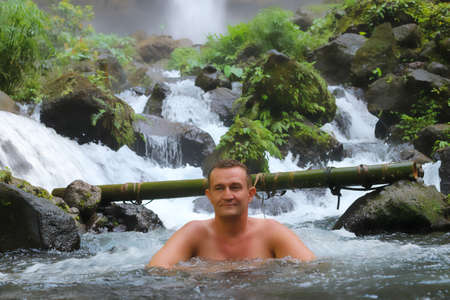Happy middle aged man resting in stream canyon river in the mountains, nature pool. Cold water, hardening and natural spa procedure, wildlife and green tourism, active healthy lifestyle, summertimeの写真素材