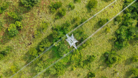 Aerial top down view high voltage steel power pylons in green field countryside. Flight over power...