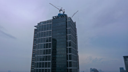 Crane and building under construction against cloudy sky