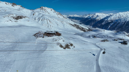 Tourists riding the Piz Nair cable car gondola over the snowy earth on the mountainside, with Lake St. Moritz under alpine mountains and Pontresina village in Engadin Valley, Grisons, Switzerland.の写真素材