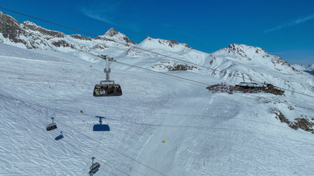Tourists riding the Piz Nair cable car gondola over the snowy earth on the mountainside. St. Moritz under alpine mountains and Pontresina village in Engadin Valley, Grisons, Switzerland.の写真素材