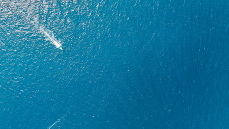 Aerial view of a boat sailing over blue water and leaving a trail of white bubbles