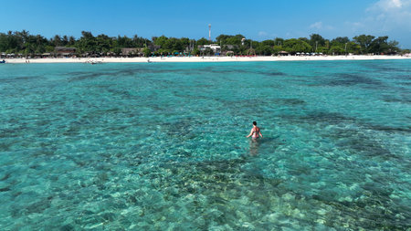 A woman in a swimsuit walked in the shallow sea waters of the beach. Woman walks through shallow waterの写真素材