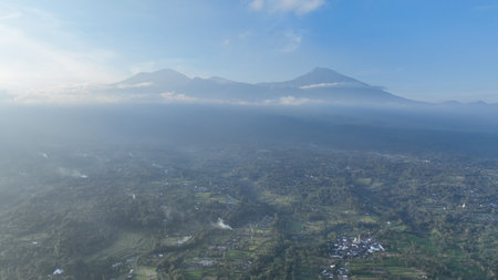 Endless green landscapes and peaceful villages unfold below, while the powerful volcano Rinjani towers in the background, its peak shrouded in mystical morning mistの写真素材