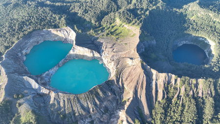 Aerial perspective reveals the striking trio of Kelimutu colored lakes nestled among lush highland forests and rugged volcanic ridgesの写真素材