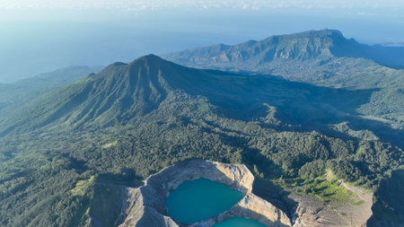 Shadowy forests and volcanic ridges create dramatic patterns across Flores, revealing an endless sea of green under a crystal blue skyの写真素材