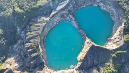 Turquoise waters fill two craters in mesmerizing contrast with surrounding rugged terrain and dense forest, creating a dramatic volcanic sceneの写真素材