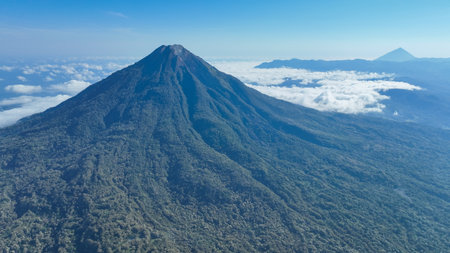 The powerful cone of a volcano dominates the horizon, surrounded by drifting clouds and endless...