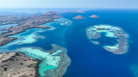 Rugged Komodo shores meet turquoise lagoons and distant atolls under clear skies