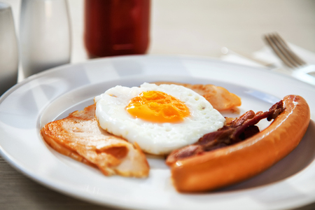 Breakfast set eggs, ham, sausage and bacon under morning light (selective focus)の写真素材