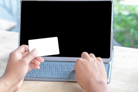 Close-up of person holding empty credit card or business card and forefinger touching keyboard of a...
