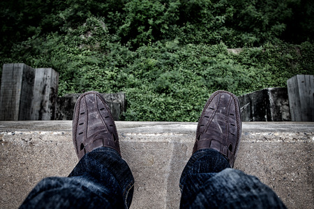 Suicide concept., Depressed young man looking down at his shoe and contemplating suicide., On the edge of a high bridge with forest below.の写真素材