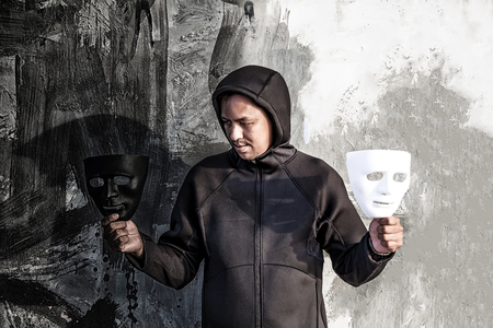 Asian man chooses between black and white mask in scary abandoned building, Human face expression, Good and Bad temptation concept.の写真素材