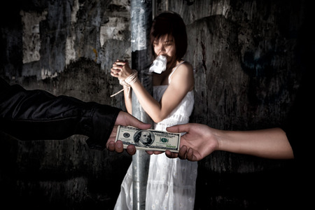 Human trafficking concept., Person hand with a dollar banknote buying victim woman in pain and bound hands with rope., missing kidnapped., in dark tone.の写真素材