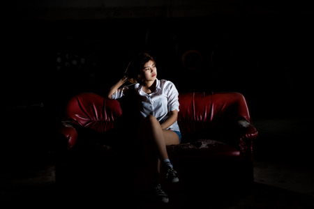 Unhappy lonely depressed woman sitting on old couch and contemplating suicide, in scary abandoned building, Concept of unemployed, sadness, depression, broken heart and human problem in dark tone.の写真素材