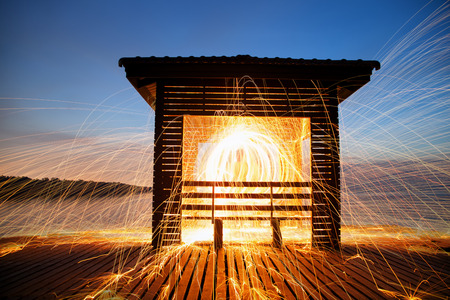 Hot Golden Sparks Flying from Man Spinning Burning Steel Wool on Wooden Bridge Extended into the Sea., Long Exposure Photography using Steel Wool Burning.の写真素材