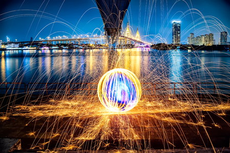 Hot Golden Sparks Flying from Man Spinning Burning Steel Wool under Bhumibol Bridge in Bangkok Thailand., Long Exposure Photography using Steel Wool Burning.の写真素材