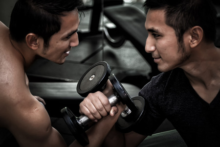 Two Asian men use dumbbell exercise weight-lifting arm-wrestle compete in fitness gymの写真素材