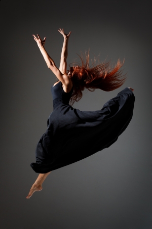 young beautiful dancer with red hair jumping on a dark studio backgroundの写真素材