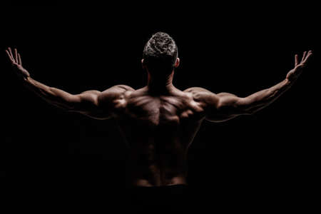 Young muscular bodybuilder posing over black background.