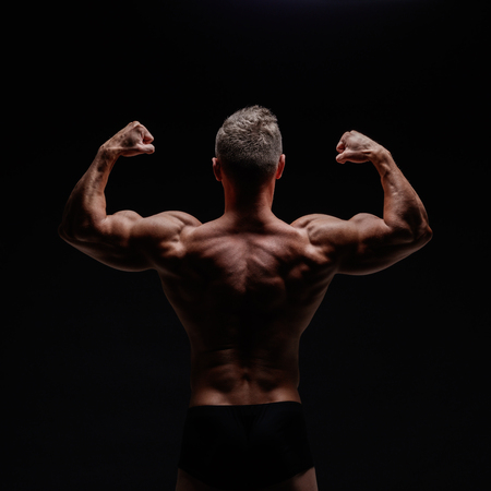 Young muscular bodybuilder posing over black background.の写真素材