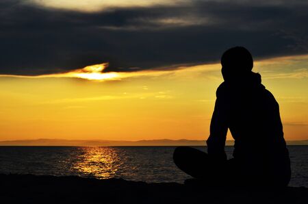 Girl sitting on the shore of the lake, and admiring the sunset. Silhouette.の写真素材