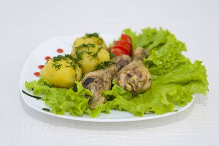 Chicken legs baked with fresh potatoes, served with vegetables.の写真素材
