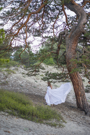 Beautiful young girl in a long white dress, walking under a big tree.の写真素材