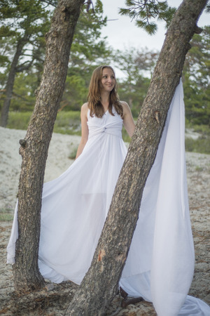 Beautiful young girl in a white dress, walking in the woods on the seashore.の写真素材