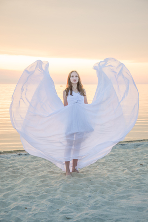 Beautiful girl dancing on the beach, her dress fluttering in the wind.の写真素材