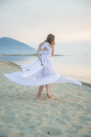 Beautiful girl dancing on the beach, her dress fluttering in the wind.の写真素材