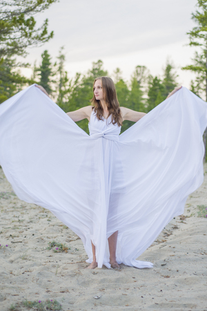 Beautiful girl dancing on the beach, her dress fluttering in the wind.の写真素材