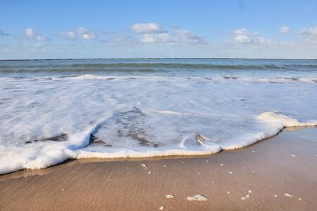 Foam of a wave at low tide on the wet sandの写真素材