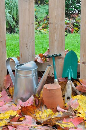 garden accessories on dead leaves in front of a wooden fence in the gardenの写真素材