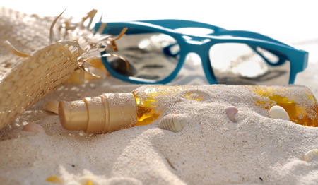 bottle of suntan oil covered by sand with hat and sunglassesの写真素材
