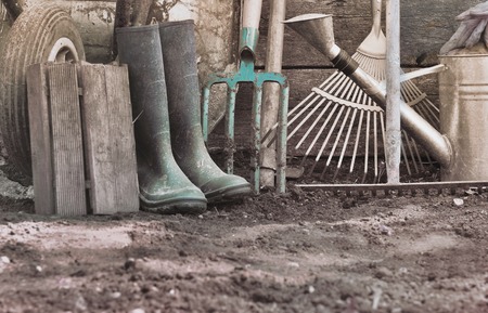 rustic gardening tools and rubber boots on the soilの写真素材