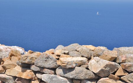 stone wall overlooking a blue seaの写真素材