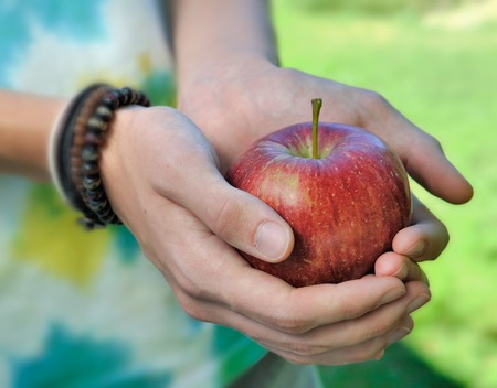 beautiful red apple held in the hands of a teenagerの写真素材